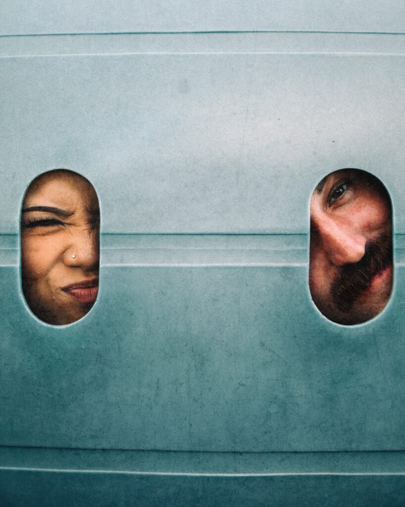 Two faces peeking through oval openings in a pale teal panel