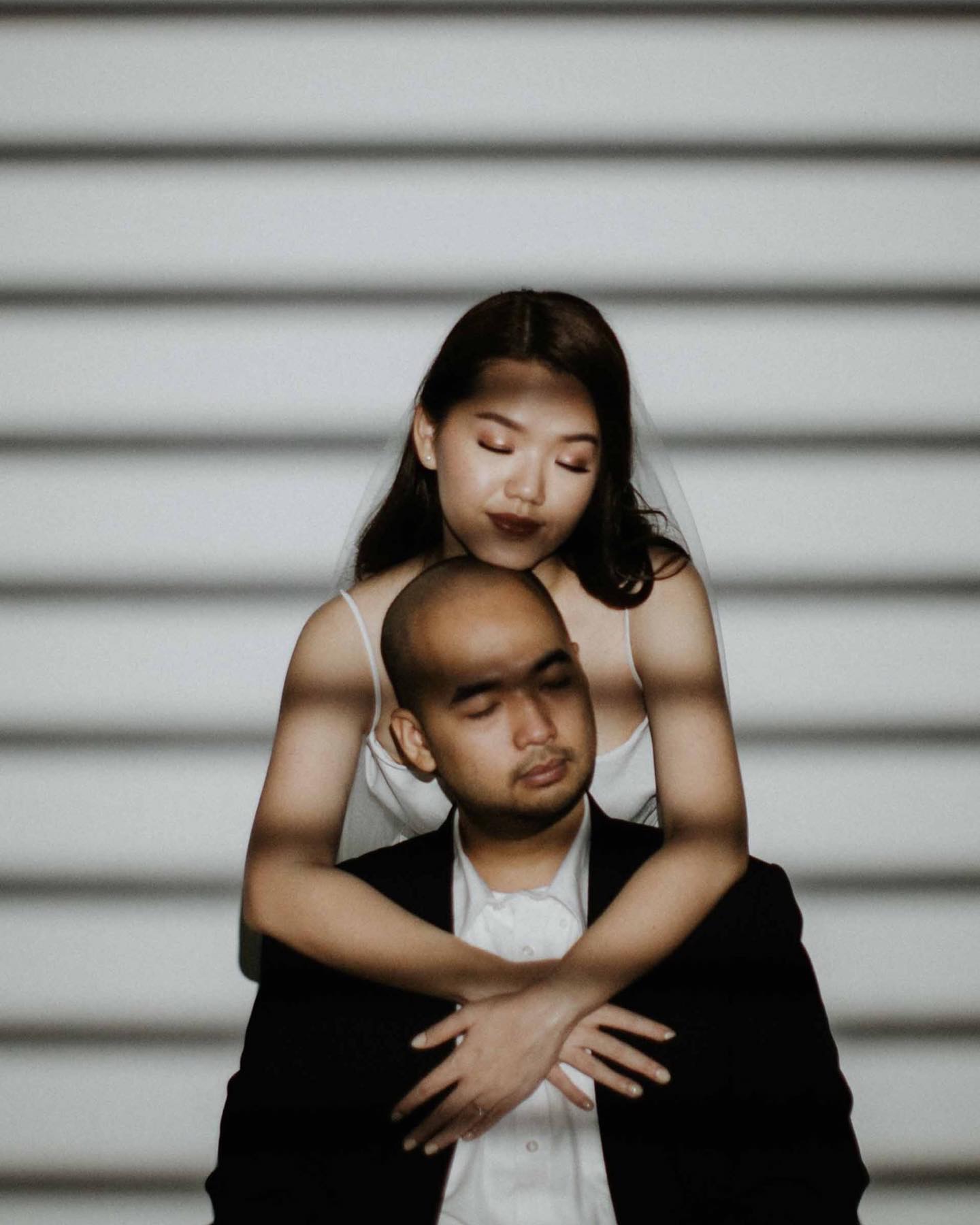 Woman embracing a seated man from behind against horizontal shadow bands