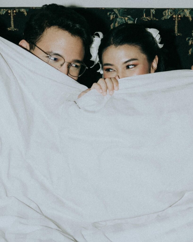 Couple looking at each other over a white sheet held in front of their faces