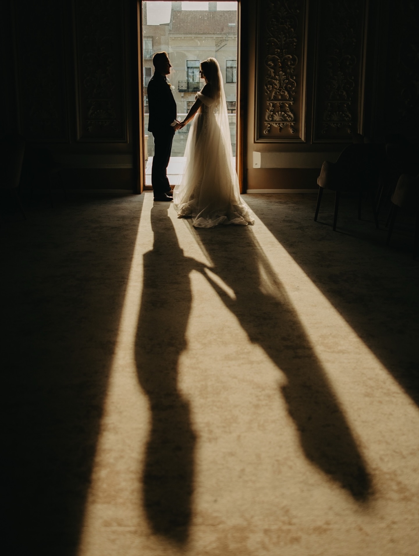 Wedding couple holding hands in a doorway with long shadows across the floor