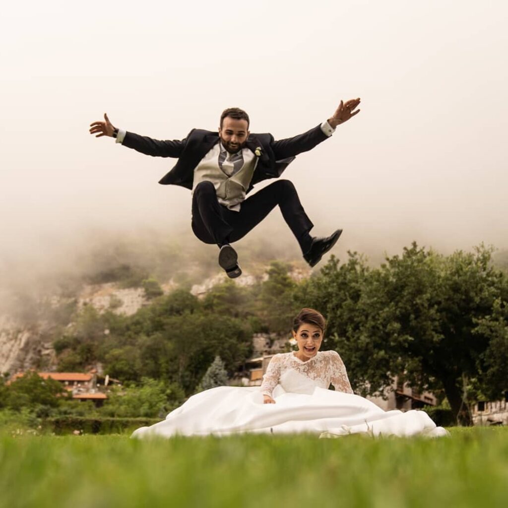 Groom jumping over a seated bride in a playful outdoor wedding portrait