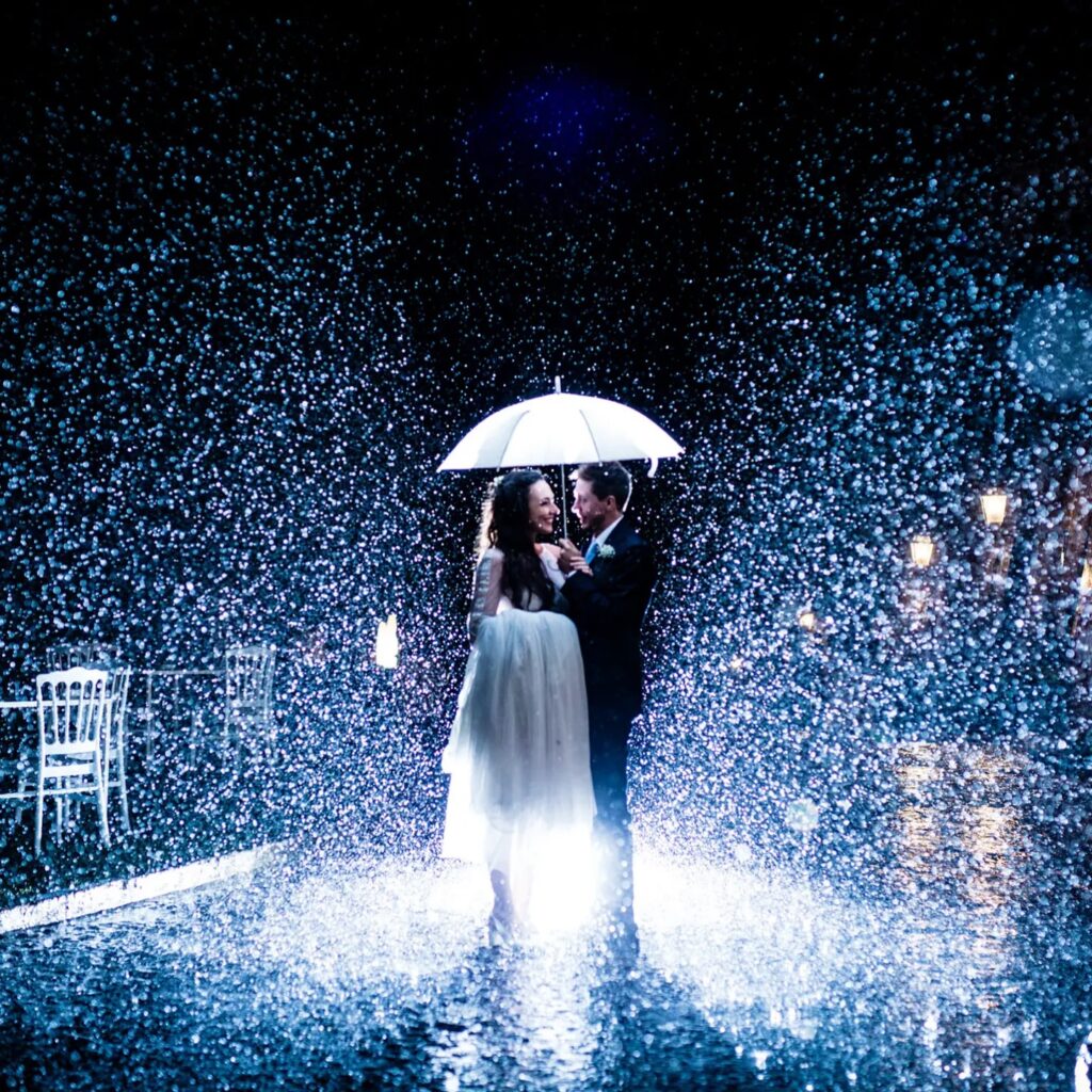 Wedding couple kissing under an illuminated white umbrella in rain at night