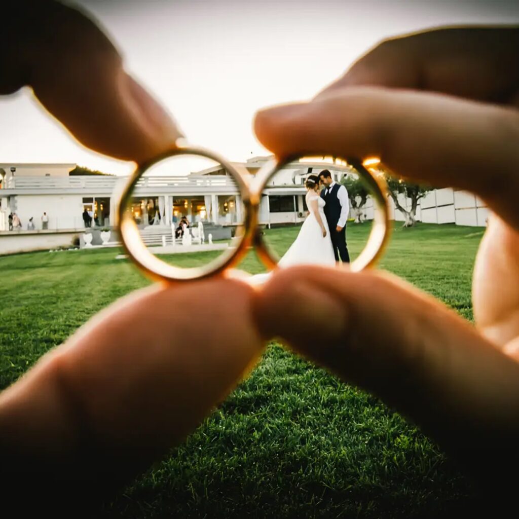 Wedding rings held close to the camera, framing a couple in the distance