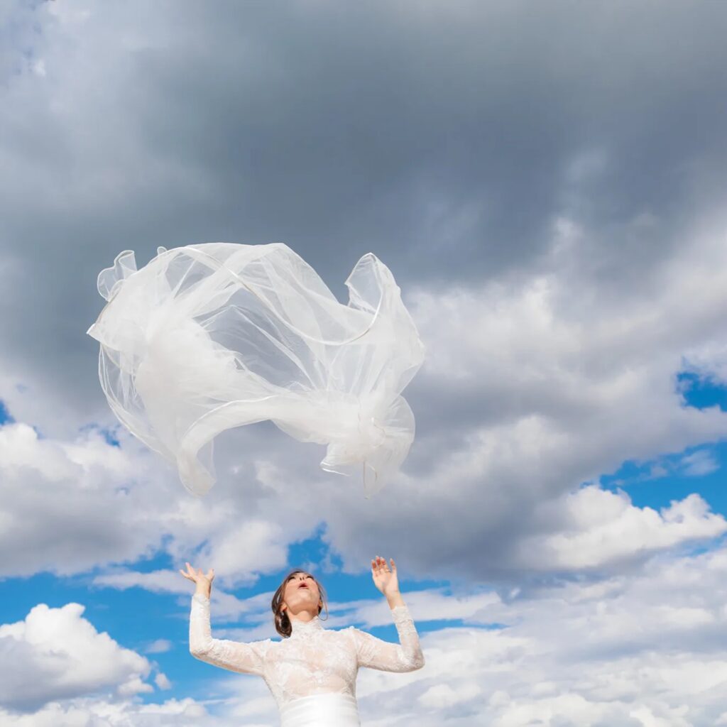Bride beneath a lifted veil against blue sky and clouds