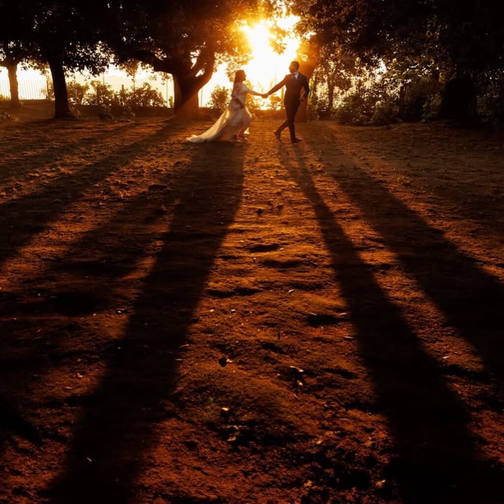 Couple holding hands on a sunlit path with long shadows behind them