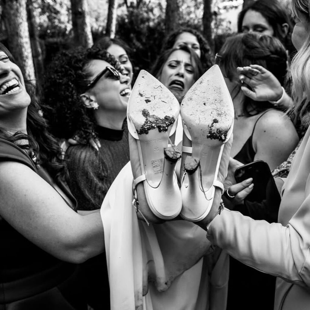 Black and white photograph of laughing wedding guests holding shoes