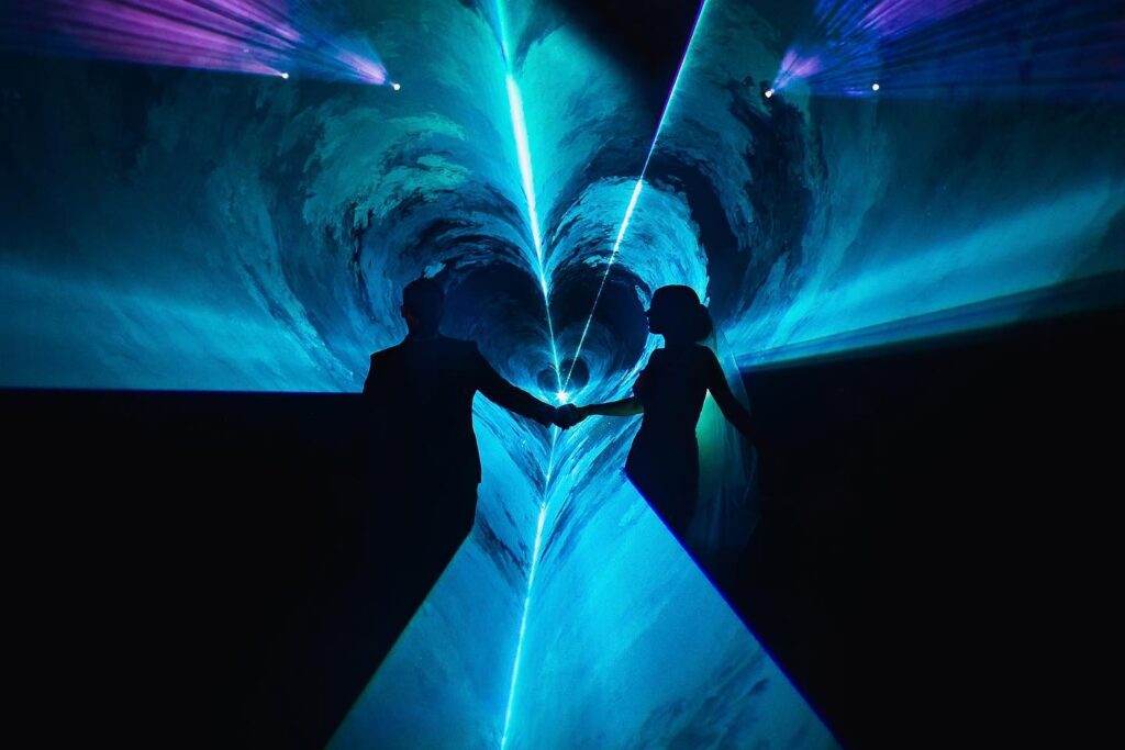Bride and partner holding hands within a blue heart-shaped light composition