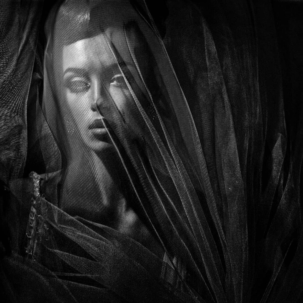 Black and white bridal face beneath layered dark mesh