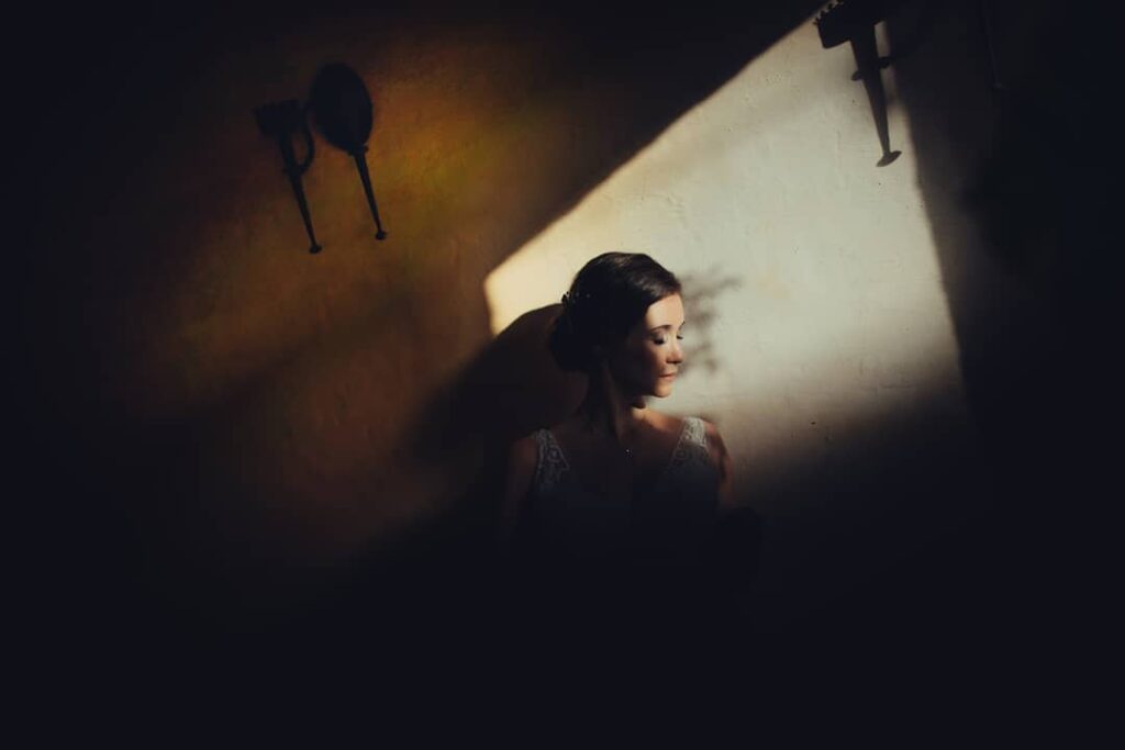 Bride in profile beside a diagonal beam of warm light on a wall