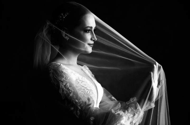 Bride in profile holding her veil against a dark background
