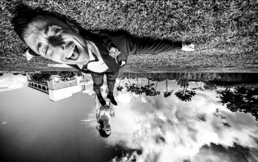 Upside-down monochrome wedding portrait with a smiling groom close to the camera