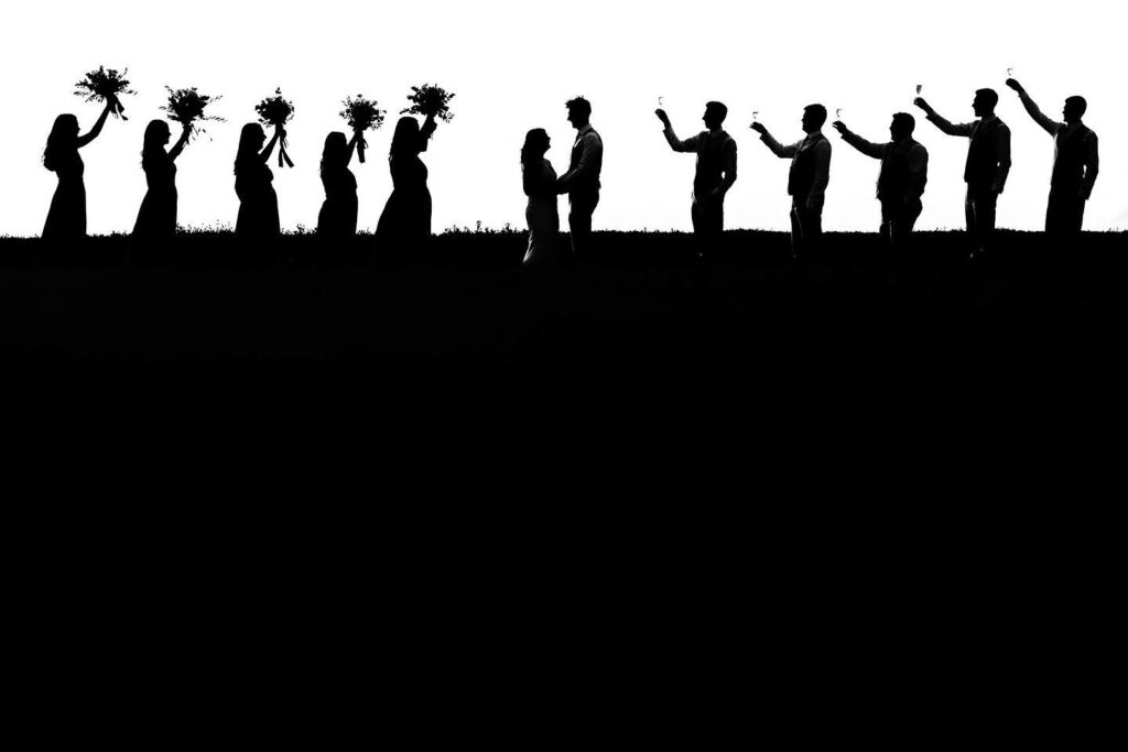 Wedding party in silhouette holding flowers along a horizontal line
