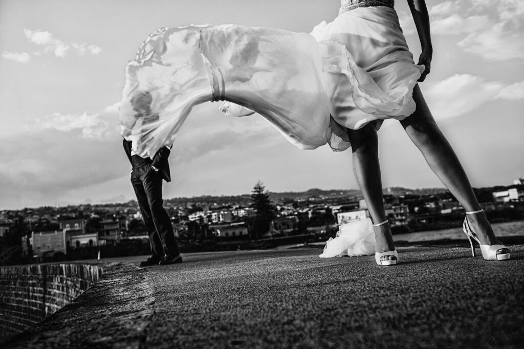 Bride's skirt sweeping across the foreground with a groom beyond on a rooftop