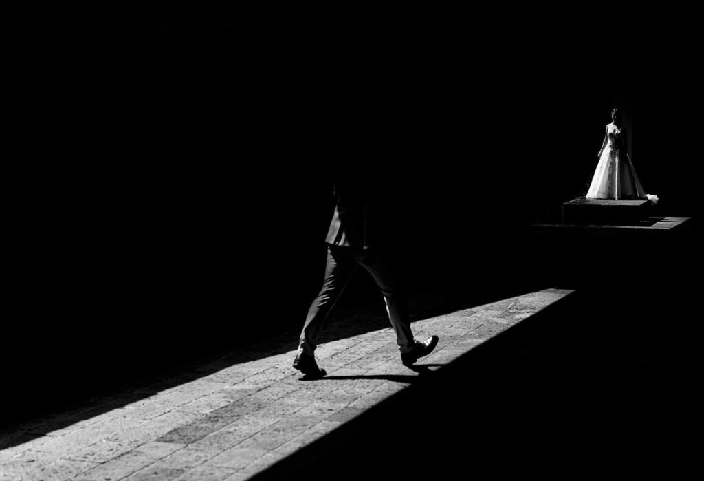 Groom crossing a diagonal patch of light toward a distant bride