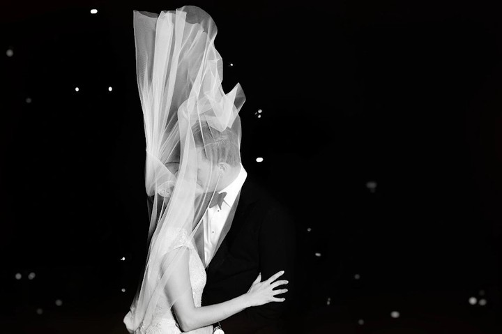 Bride with an arm extended beneath a vertically billowing veil in darkness