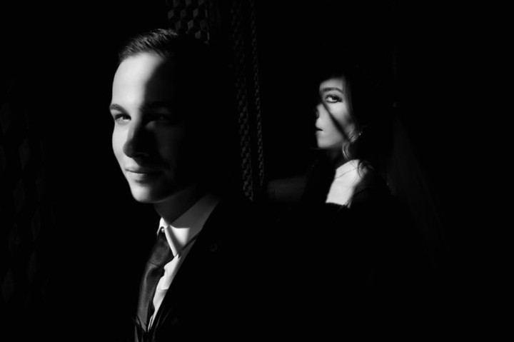 Groom in the foreground and bride behind, their faces isolated by light