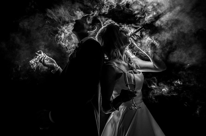 Couple back to back with a cigar, a glass and illuminated smoke in monochrome