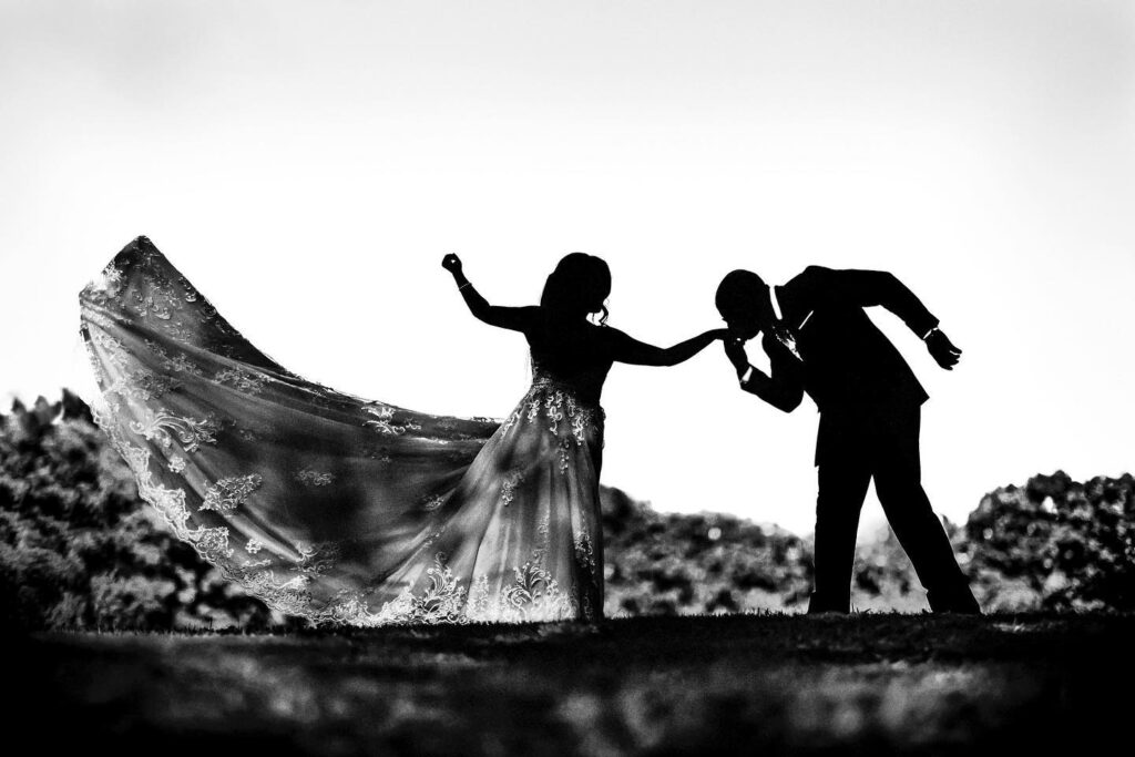 Groom kissing the bride's hand as her dress sweeps outward in silhouette