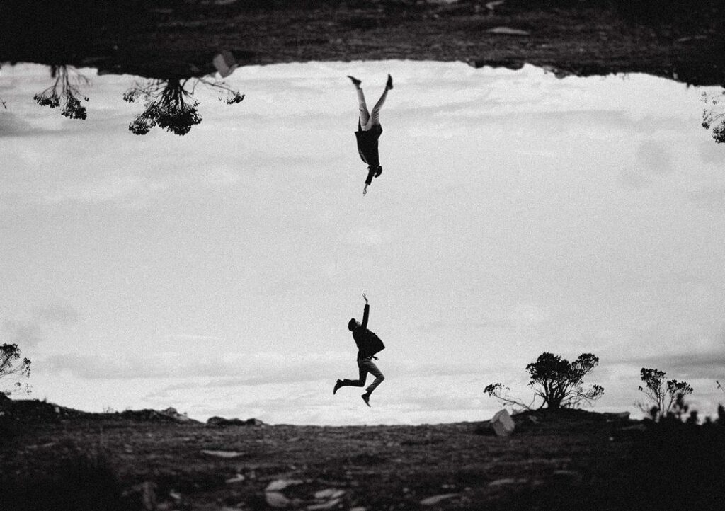 Two airborne figures mirrored across a monochrome landscape
