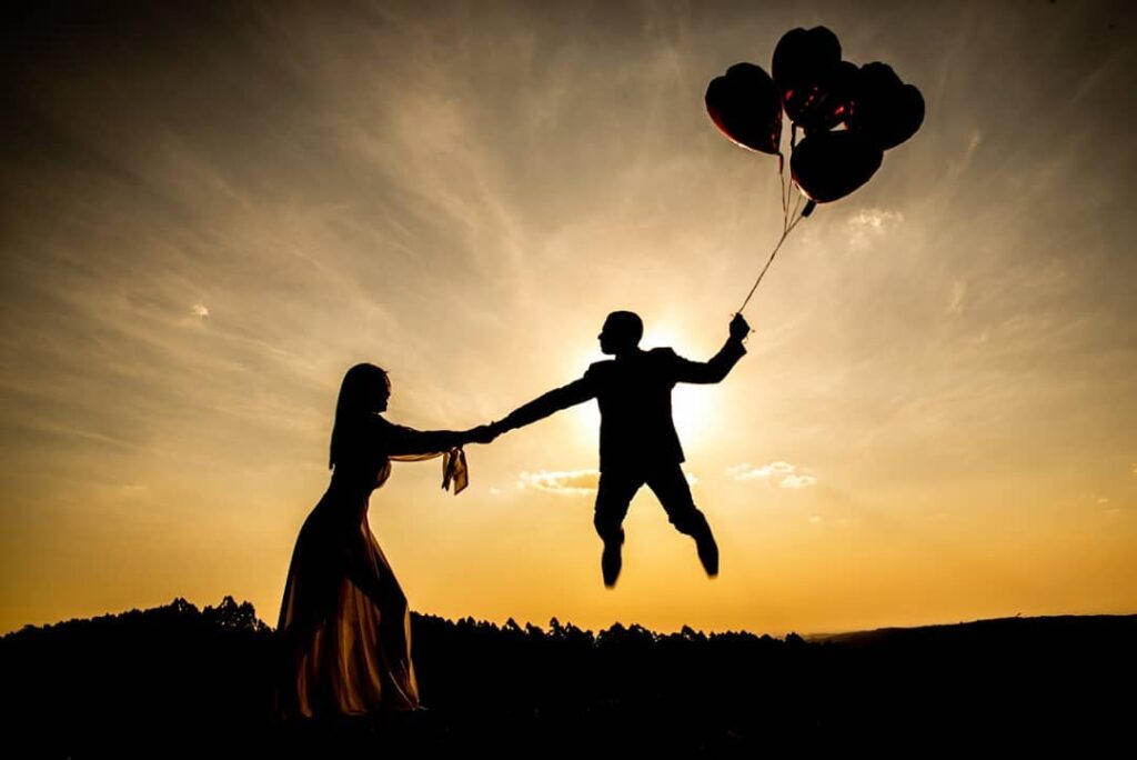 Silhouetted couple holding hands with balloons above the airborne groom