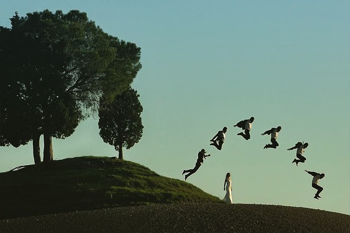 Repeated airborne groom shapes forming an arc over a bride on a hillside