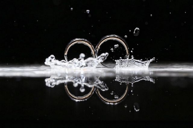 Wedding rings surrounded by a splash and their reflection in black and white