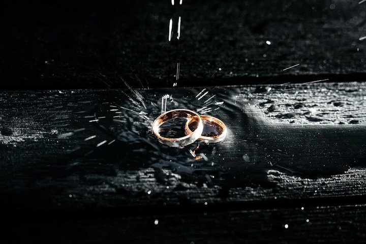 Gold wedding rings on a dark wet surface beneath falling drops