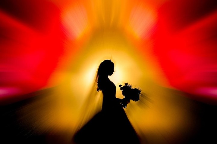 Bride holding a bouquet in silhouette against red and yellow light
