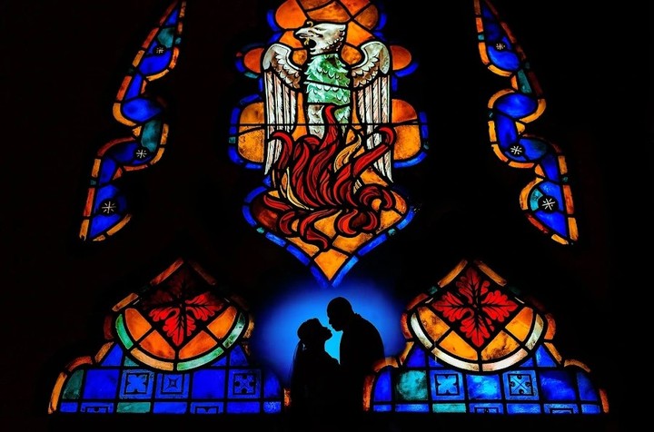 Couple in silhouette beneath a colorful stained-glass window