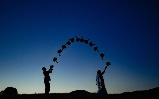 Two wedding silhouettes beneath an arc of bouquet shapes in a blue evening sky