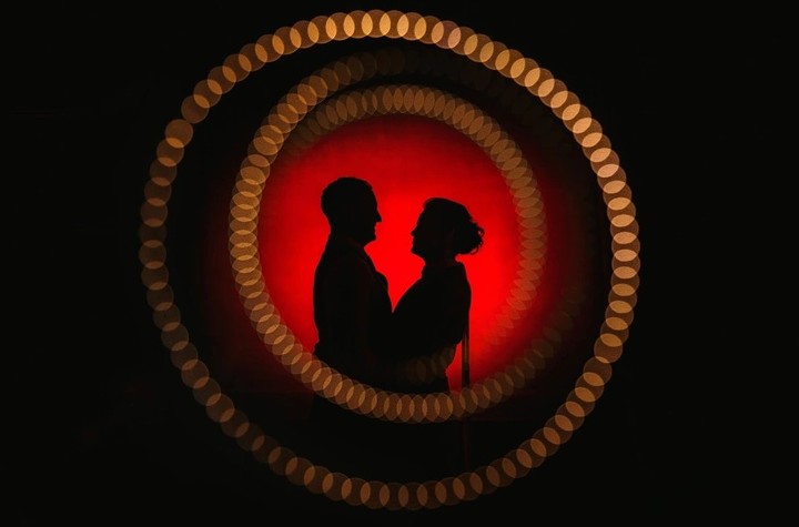 Couple facing each other in silhouette inside a red and gold circle of light