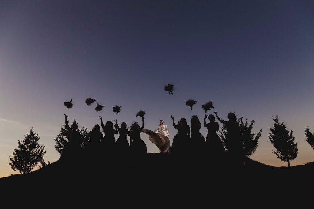 Wedding party raising flowers in silhouette along a ridge at dusk