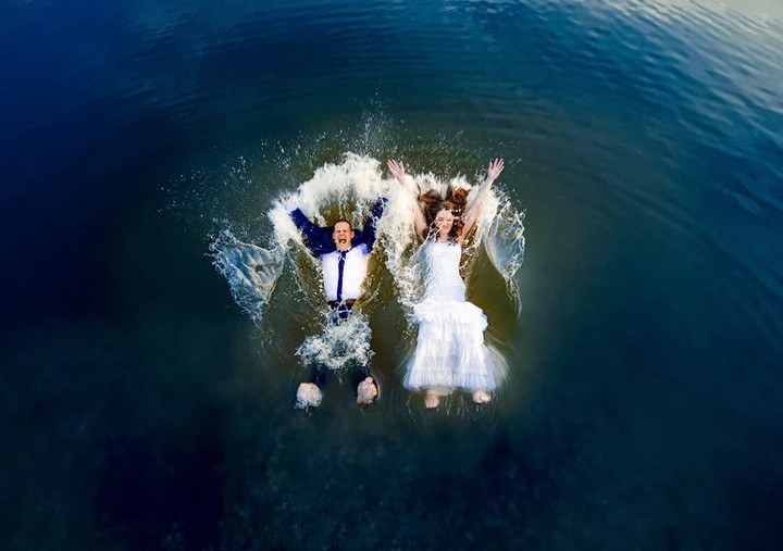 Overhead view of a wedding couple splashing into dark blue water