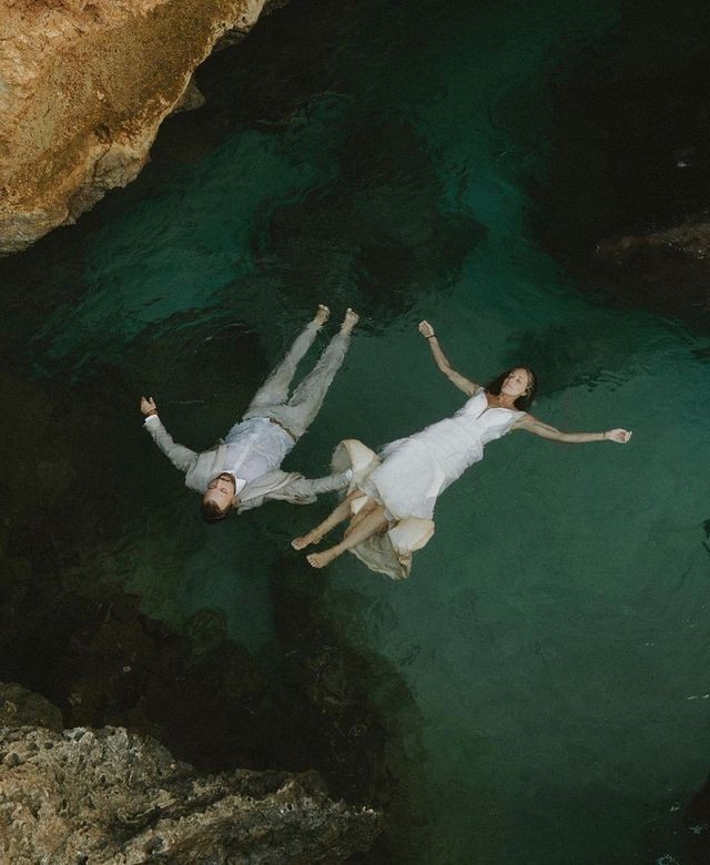 Overhead view of a couple floating hand in hand in a dark green rock pool