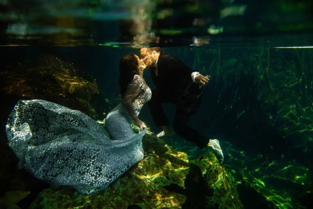 Wedding couple embracing underwater among green reflections and rocks