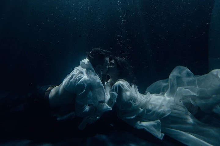 Couple embracing in dark blue water with white fabric floating around them