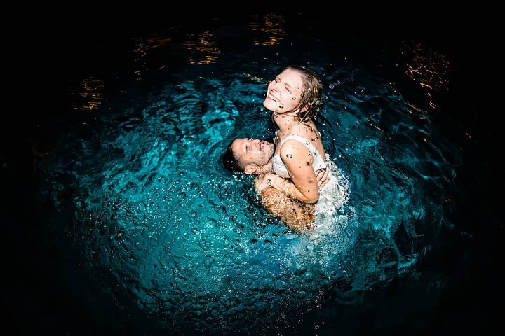 Laughing couple embracing in a pool surrounded by blue splashes