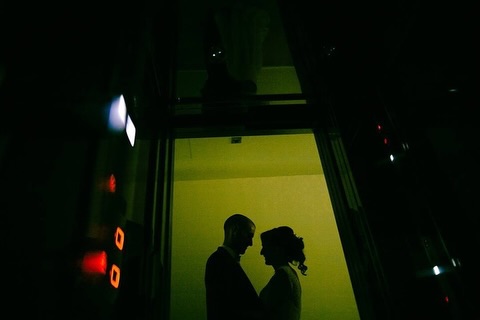 Couple silhouetted in a green-lit doorway against dark surroundings