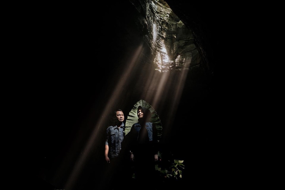 Couple standing beneath a shaft of light inside a dark rocky opening