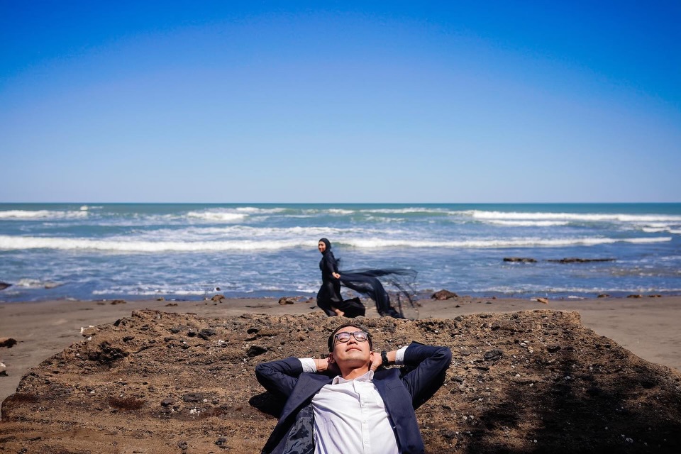 Man reclining in the foreground of a beach portrait with his partner near the sea