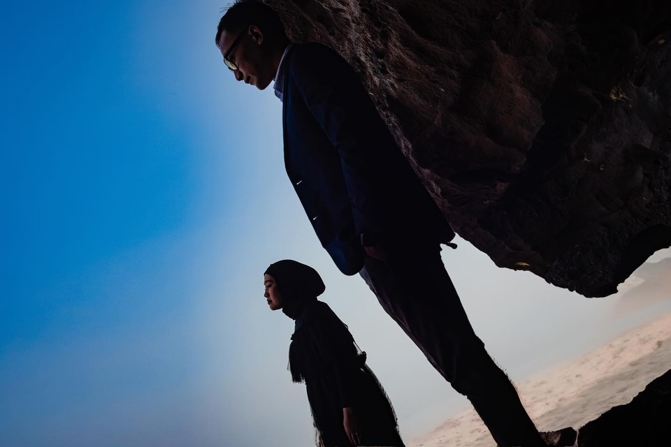 Tilted portrait of a couple beside a large rock against blue sky