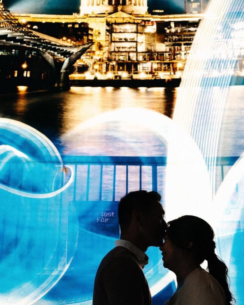 Couple kissing at night beneath turquoise light trails near Tower Bridge