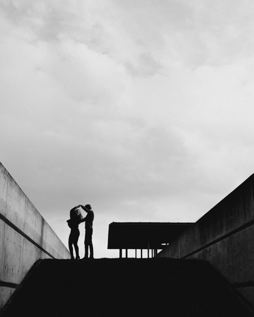 Small silhouetted couple at the top of steps beneath a broad pale sky