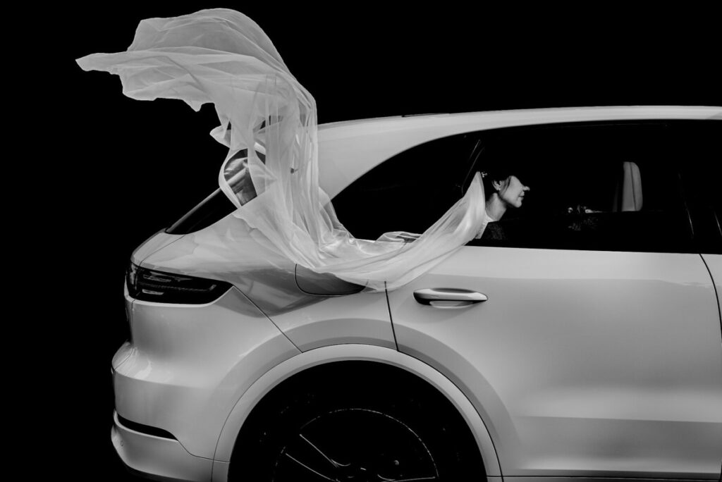 Retrato en blanco y negro de una novia en la ventanilla de un coche, con el velo formando una gran curva sobre el vehículo