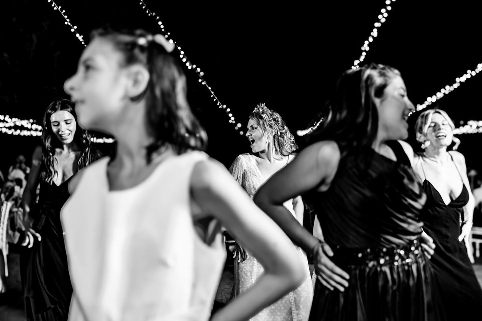 Invitados bailando bajo guirnaldas de luces, con una niña en primer plano, en blanco y negro