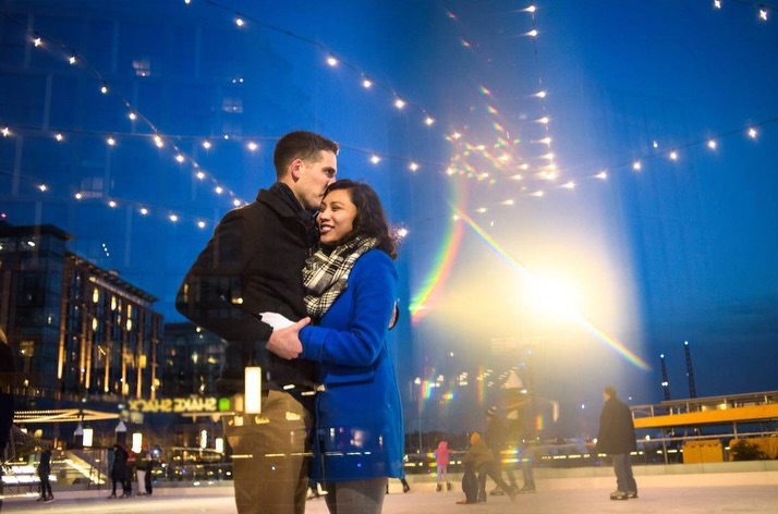 Pareja abrazada bajo luces urbanas mientras uno besa al otro en la frente