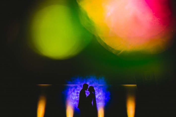 Silueta de una pareja de boda bajo grandes círculos de luz rosa, amarilla y verde