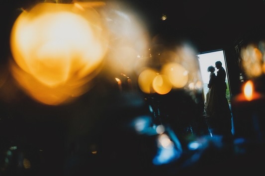 Silueta de una pareja en una puerta luminosa, más allá de luces doradas desenfocadas en primer plano
