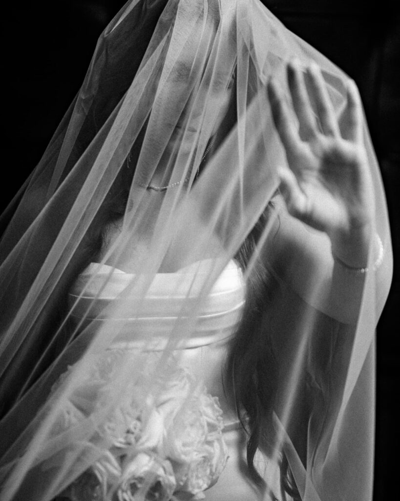 Black and white bridal portrait behind a veil with one hand raised