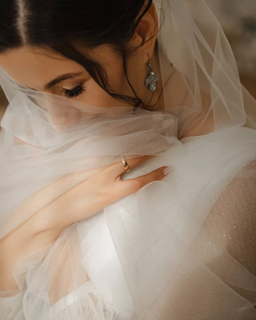 Retrato cercano de una novia con luz cálida, un velo sobre la parte inferior del rostro y una mano visible